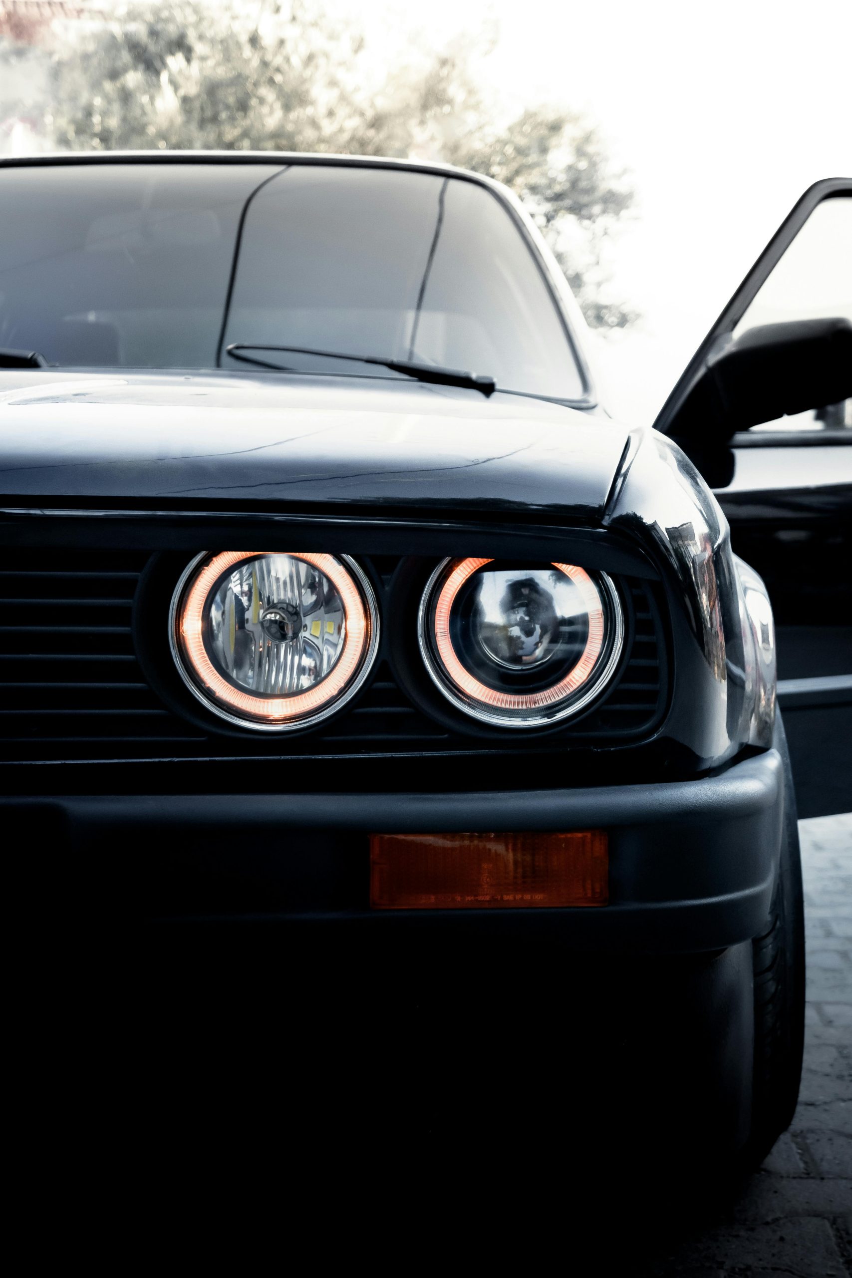 Gros plan d'une BMW E30 vintage mettant en valeur ses phares circulaires emblématiques.