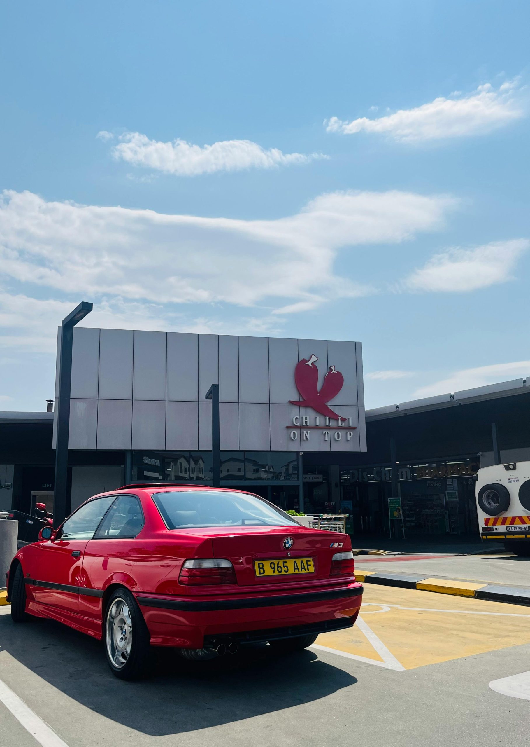 Vibrante BMW coupé rouge garée devant un bâtiment moderne sous un ciel bleu dégagé.