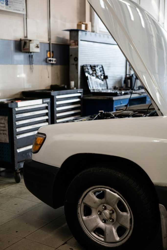 White car with hood open in a professional auto repair shop. Toolbox and equipment visible. Voiture blanche avec capot ouvert dans un atelier de réparation automobile professionnel. Boîte à outils et équipement visibles.