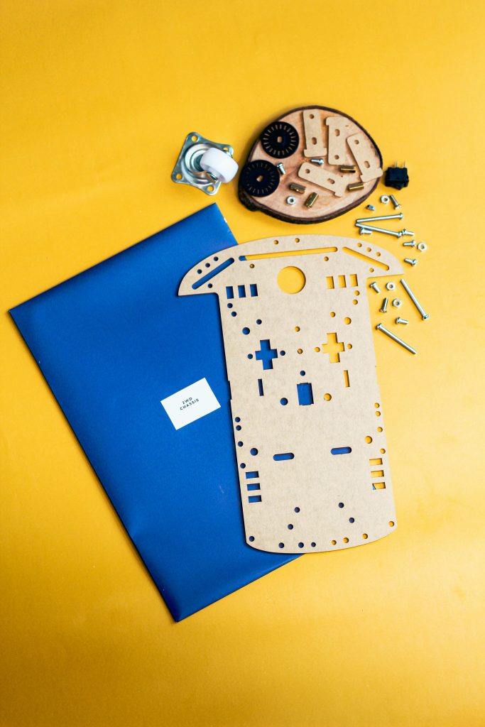 Flat lay of DIY robotics kit with gears and frame on a vibrant yellow surface. Mise à plat d'un kit de robotique DIY avec engrenages et cadre sur une surface jaune vif.
