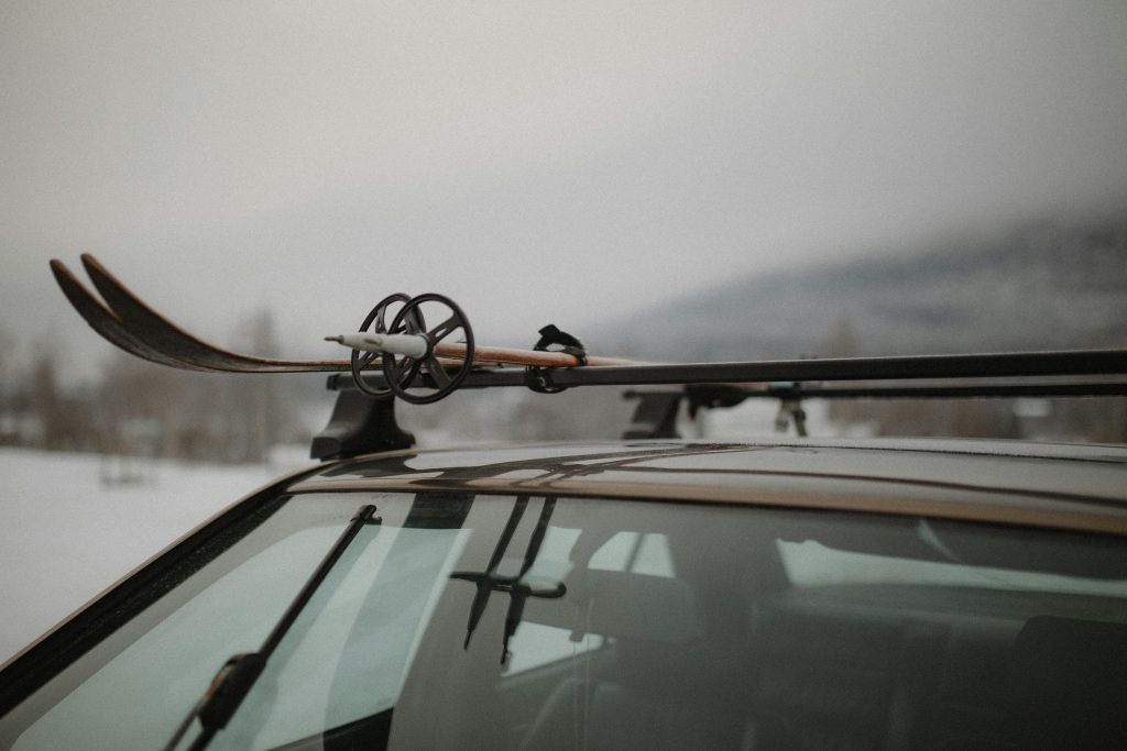 Close-up of skis and poles on a car roof rack in a snowy winter setting, ready for adventure. Gros plan sur des skis et des bâtons sur un porte-skis de voiture dans un cadre hivernal enneigé, prêt pour l'aventure.
