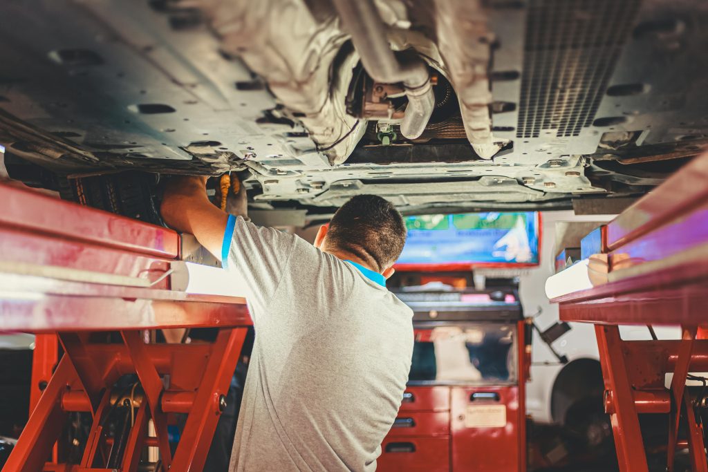 A mechanic works under a lifted car in an auto repair shop, adjusting parts. Un mécanicien travaille sous une voiture soulevée dans un atelier de réparation automobile, en ajustant les pièces.