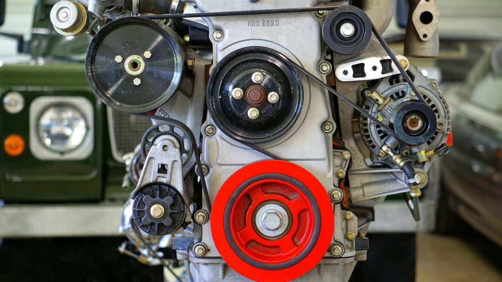 Detailed view of a car engine showcasing belts and colorful pulleys in a workshop setting. Vue détaillée du moteur d'une voiture présentant des courroies et des poulies colorées dans un atelier.
