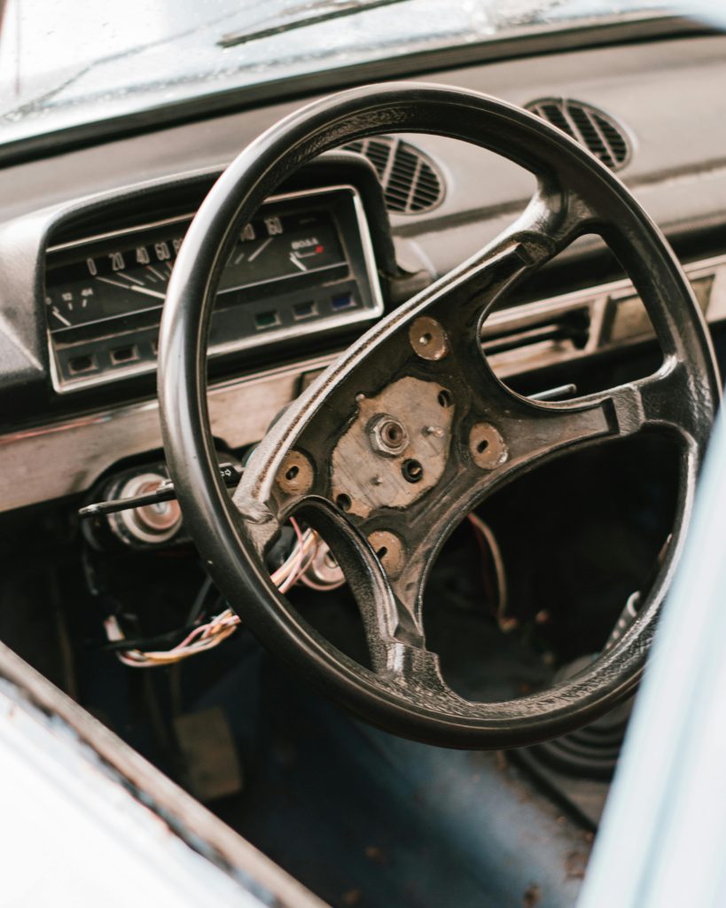 A detailed close-up of a vintage car's dashboard and steering wheel missing the center plate, evoking a sense of nostalgia. Gros plan détaillé sur le tableau de bord et le volant d'une voiture vintage dont le cache du moyeu est absent, évoquant un sentiment de nostalgie.