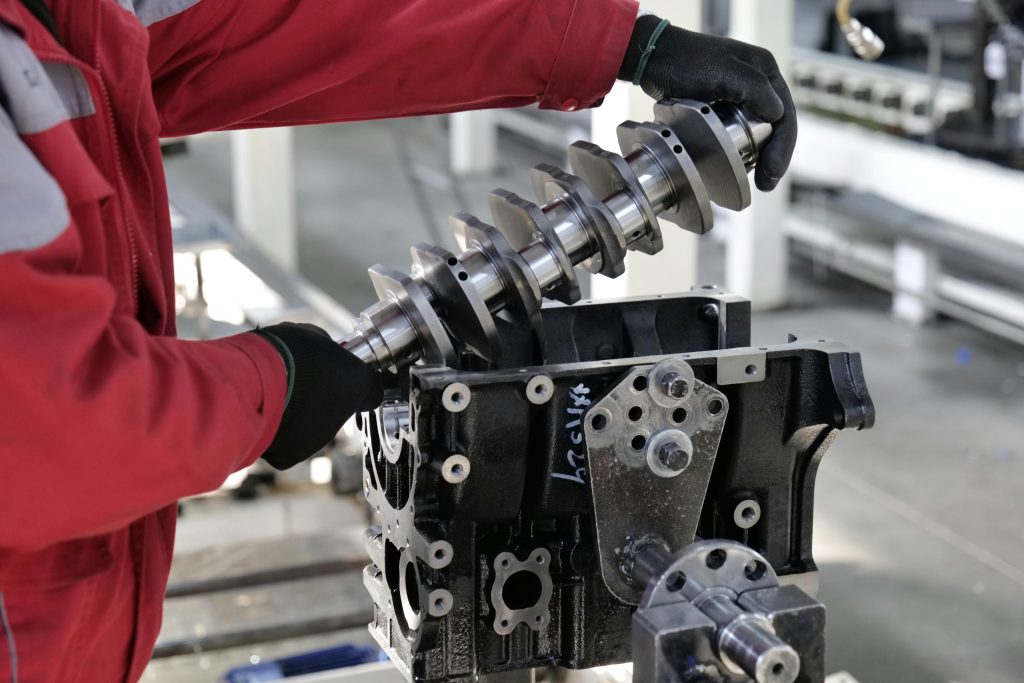 Mécanicien travaillant sur l'installation d'un vilebrequin dans un bloc moteur dans un environnement industriel.