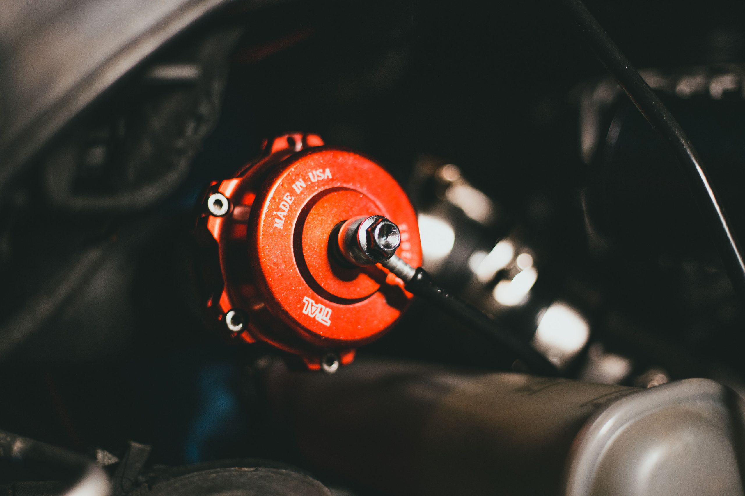 Detailed view of a red valve in a car engine, highlighting precision engineering. Vue détaillée d'une vanne rouge dans un moteur de voiture, mettant en évidence la précision de l'ingénierie.