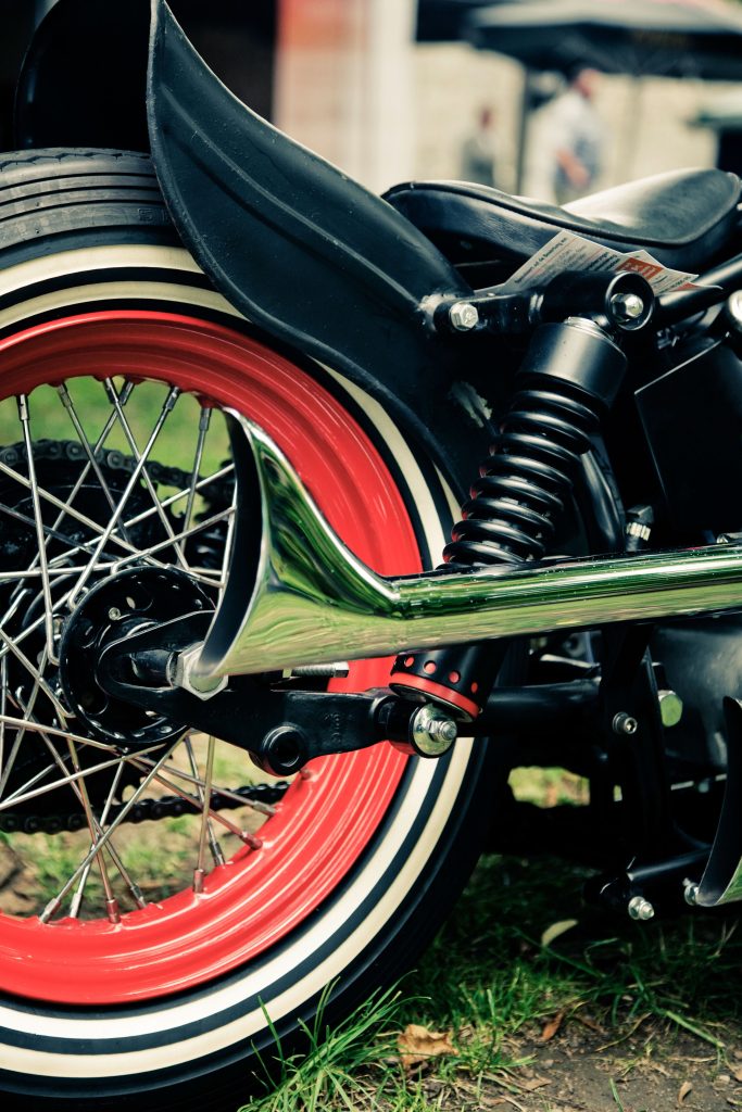Detailed view of a retro motorcycle with vibrant red wheel rim and chrome exhaust. Vue détaillée d'une moto rétro avec une jante de roue rouge éclatant et un échappement chromé.