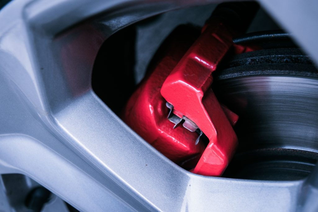 Detailed photo of a red automotive brake caliper and disc brake in focus. Photo détaillée d'une pince de frein automobile rouge et d'un disque de frein au foyer.