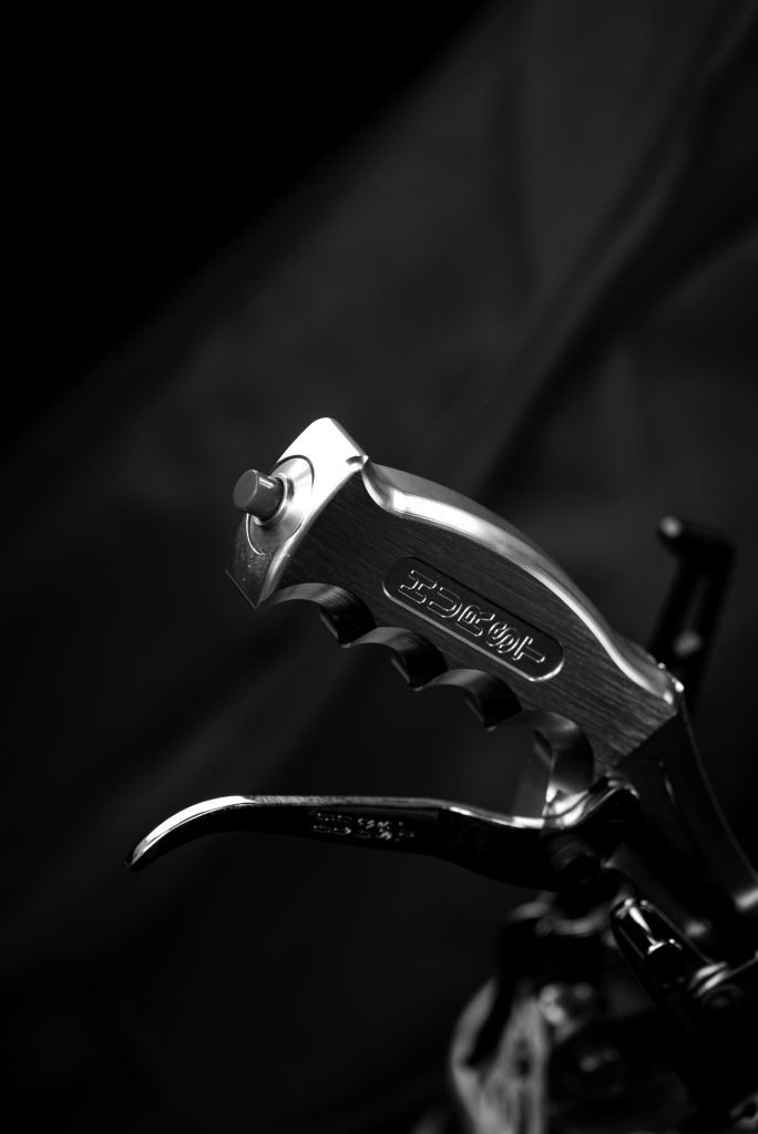Detailed black and white shot of a metal motorcycle lever with intricate details. Gros plan en noir et blanc d'un levier de moto en métal avec des détails complexes.