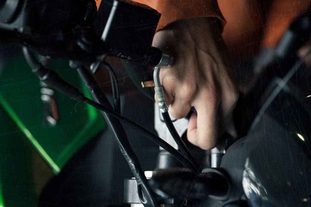 A detailed close-up of a hand adjusting motorcycle cables, showcasing technical maintenance. Un gros plan détaillé d'une main ajustant les câbles d'une moto, mettant en évidence la maintenance technique.