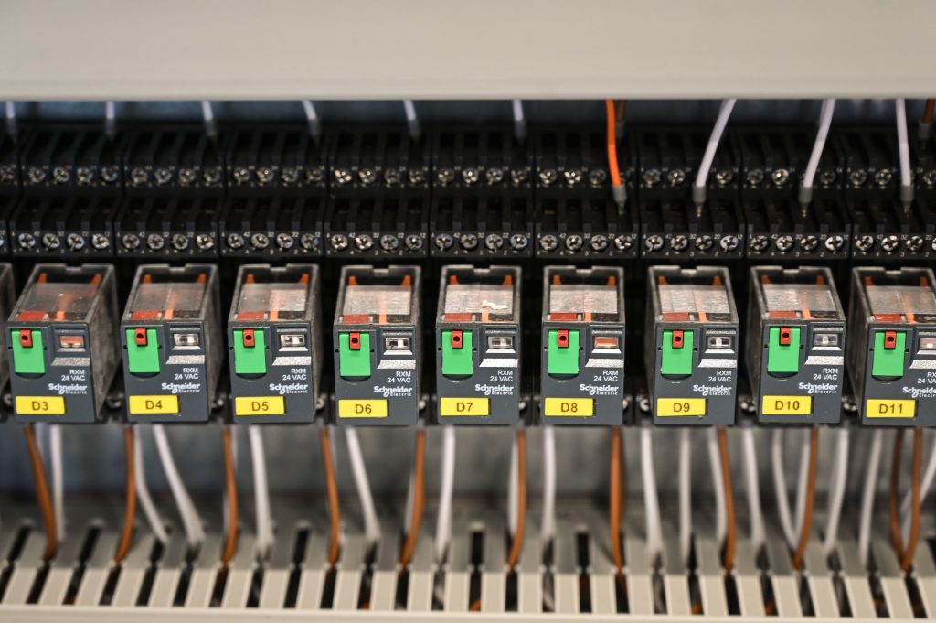 Close-up view of electrical relays in an industrial panel box showcasing circuit components. Vue rapprochée de relais électriques dans un boîtier de panneau industriel mettant en évidence les composants du circuit.