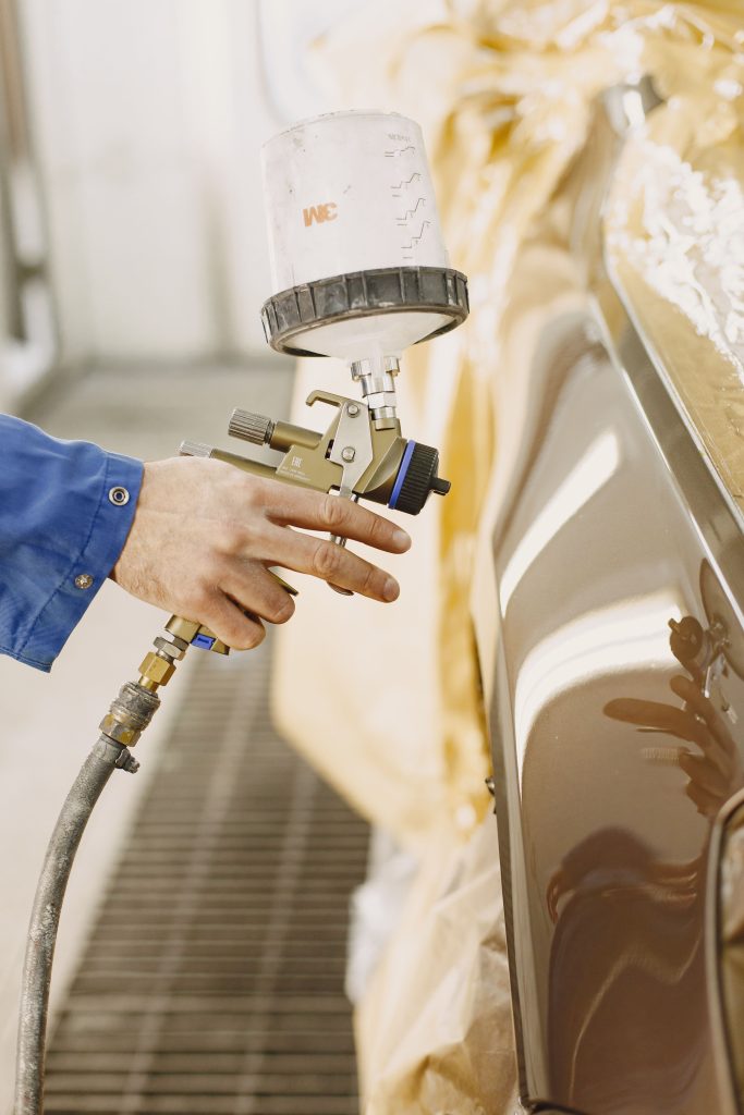 A technician spray paints a car with a paint spray gun in a workshop. Un technicien peint une voiture au pistolet de peinture dans un atelier.