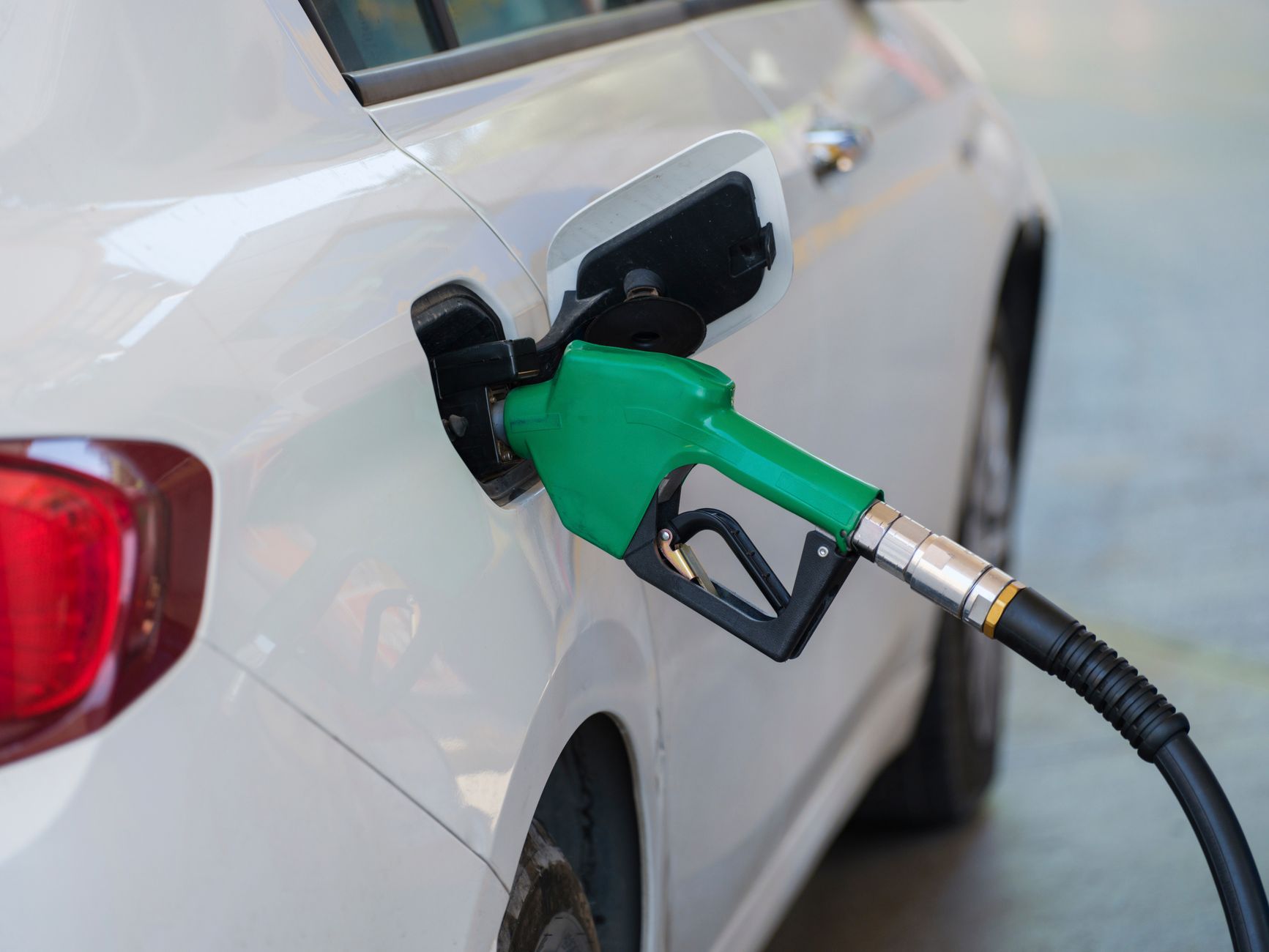 Pistolet vert de pompe à essence inséré dans le réservoir d'une voiture blanche
